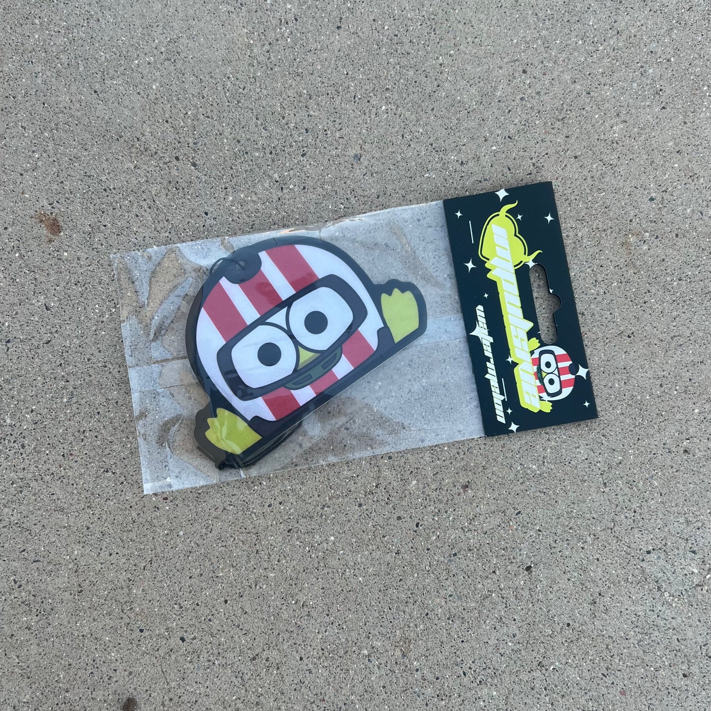 Sanrio Keroppi Green Frog Air freshener hanging from black string, wearing white and red stripe helmet. black background with stars and sparkles. Impulsive llc y2k heart logo with watermelon label cardboard head card packaging.
