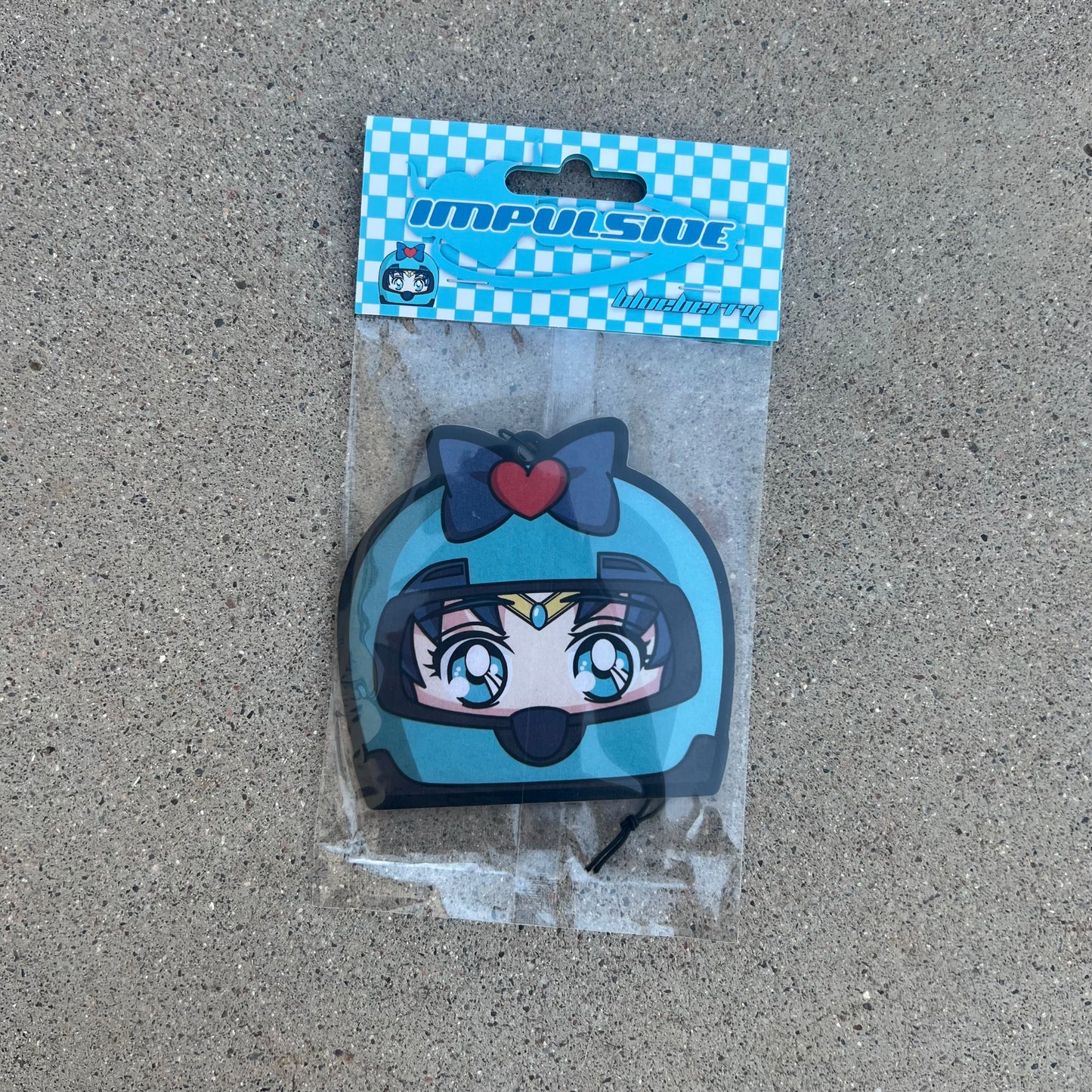 Sailor Moons friend sailor mercury air freshener hanging from black string. Wearing blue helmet with blue bow and red heart on blue eyed blue hair japanese anime girl. Blue and white checkered background with blue y2k impulsive logo and blueberry scent label cardboard head card packaging.