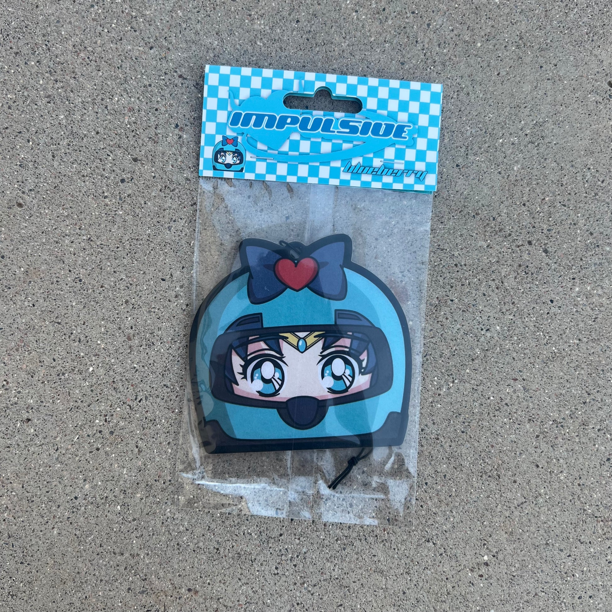 Sailor Moons friend sailor mercury air freshener hanging from black string. Wearing blue helmet with blue bow and red heart on blue eyed blue hair japanese anime girl. Blue and white checkered background with blue y2k impulsive logo and blueberry scent label cardboard head card packaging.