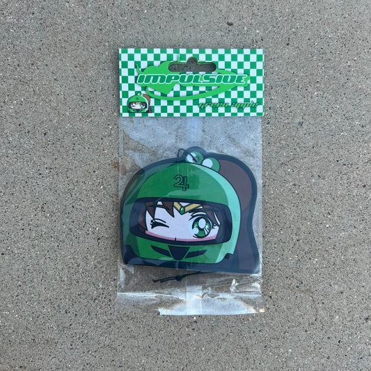 Anime Jupiter air freshener hanging from black string. Green helmet with brown hair pony tail anime japanese girl character with green eyes. Green checkered background with y2k impulsive logo and green apple scent logo cardboard head card packaging.