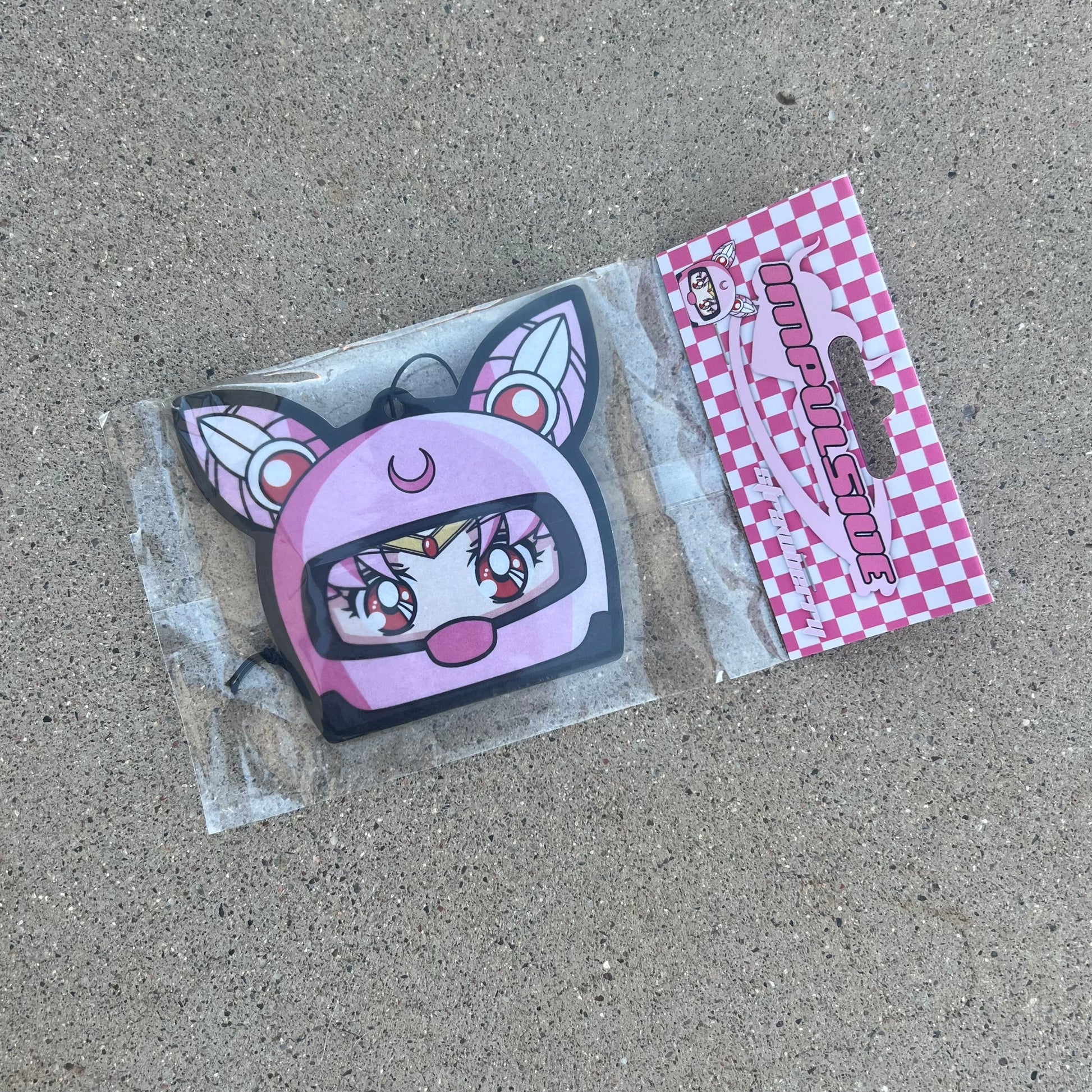 Chibi USA in pink helmet hanging from black string air freshener. Pink Checker cardboard packaging with pink y2k impulsive logo strawberry scent air freshener.