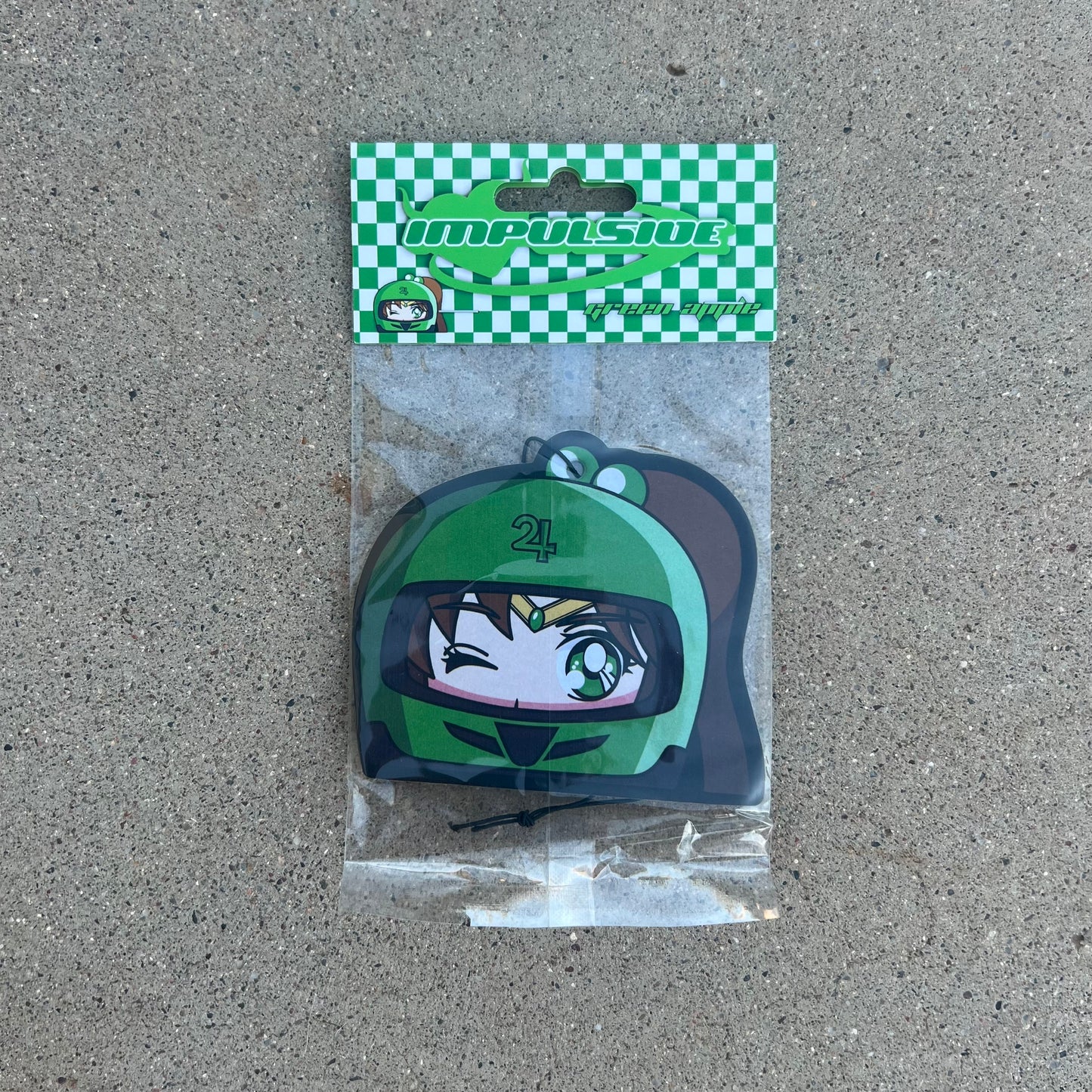 Anime Jupiter air freshener hanging from black string. Green helmet with brown hair pony tail anime japanese girl character with green eyes. Green checkered background with y2k impulsive logo and green apple scent logo cardboard head card packaging. 