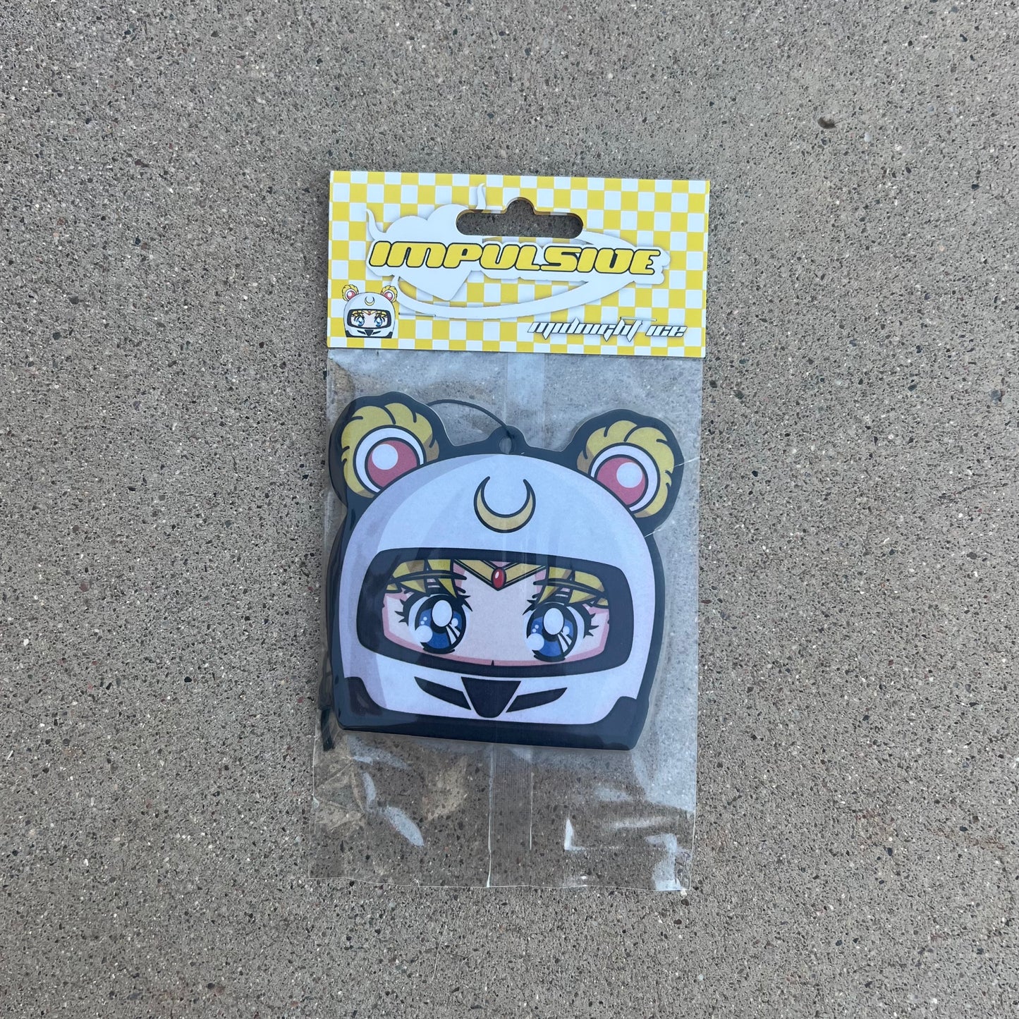 Moon Japanese Anime Character air freshener hanging from black string. Wearing white helmet with yellow moon crescent logo on blue eyed anime girl. blonde spacebuns. white and yellow checkered background with white y2k impulsive logo midnight ice scent label cardboard head card.