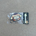 Sanrio Pompompurin Dog Racer Airfreshener hanging from black string. Cream Color dog with orange cream stripe and hat winking with paw prints on helmet. Black Background with stars and impulsive cream color y2k logo with peach label cardboard head card packaging.