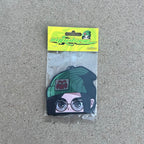 Anime Character Killjoy Lemon Scent Air freshener. Anime character, green beanie with logo, brown eyes with glasses, black hair with cuff earrings on left ear, hanging from black string. Yellow and green swirl cardboard head card packaging. Retro Y2K impulsive logo lemon label.