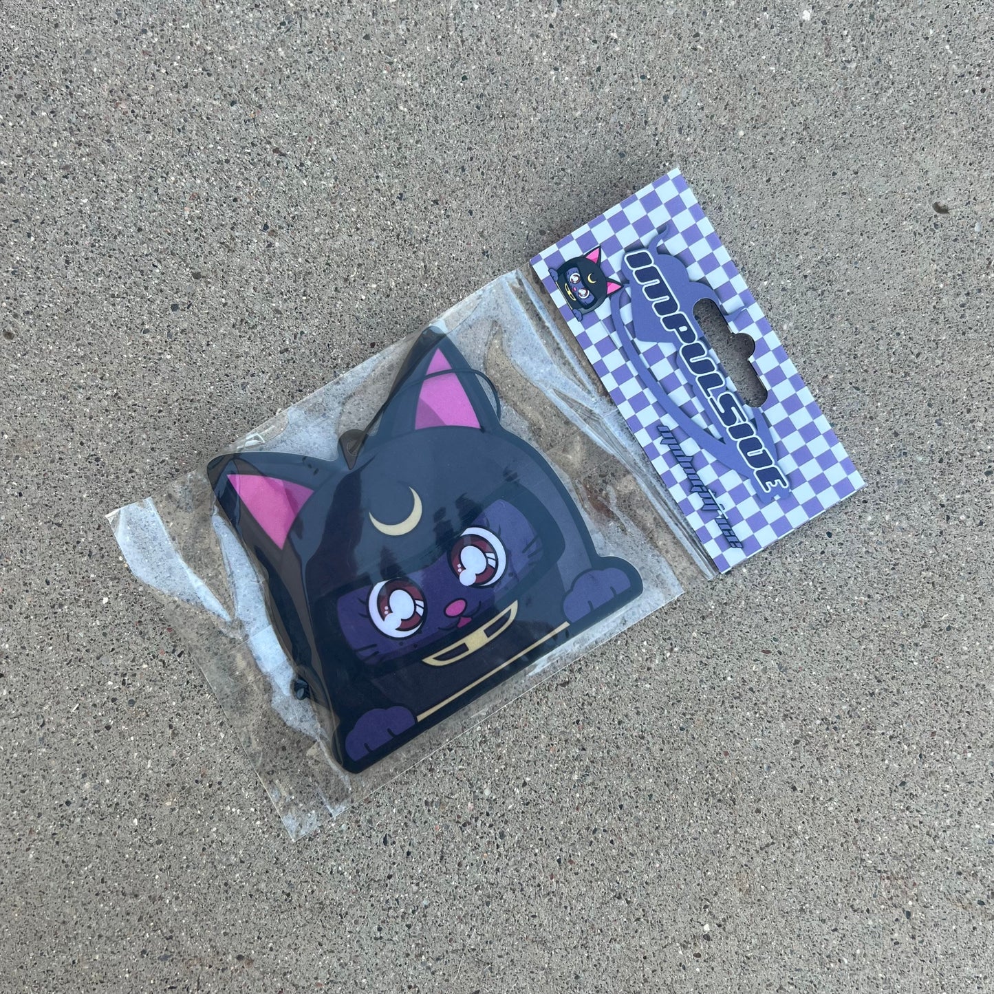 purple luna cat wearing grey helmet with moon crescent in center air freshener hanging from black string. Purple Checkered background with purple impulsive llc y2k logo midnight ice label cardboard head card packaging.
