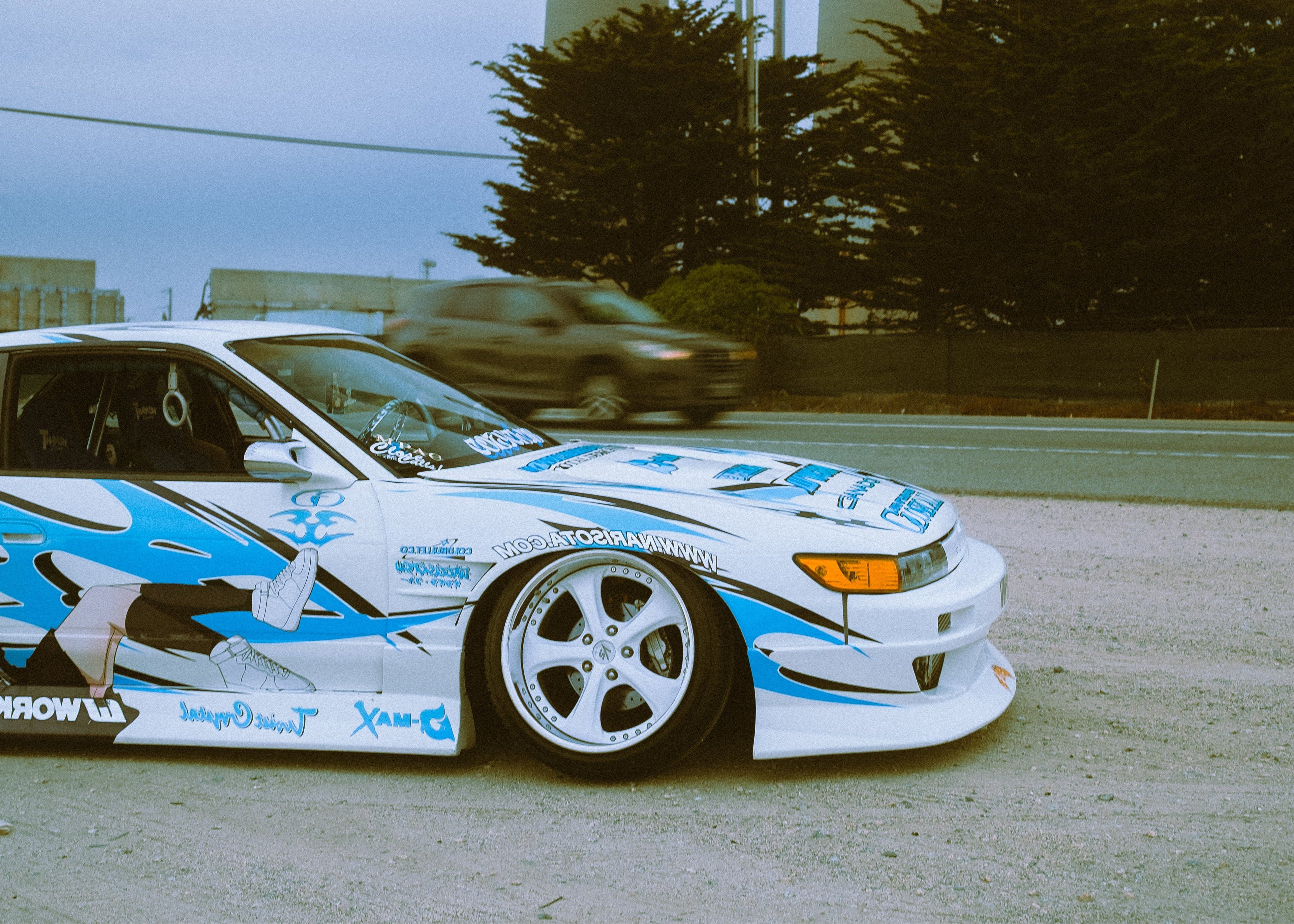 Car with a blue and white design on a road with power plants in the background
