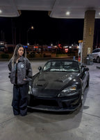 Person standing next to a black sports car honda s2000 at a gas station at night.